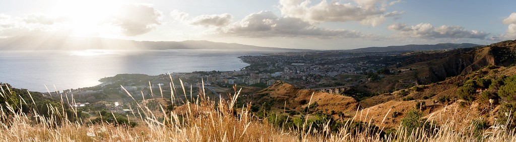 Panoramica dello Stretto e di Reggio Calabria vista dalle colline, con il sole che filtra tra le nuvole e l'erba secca in primo piano